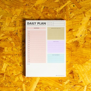 May include: A white daily planner with a pink, light blue, and beige colour scheme. The planner has sections for "Agenda", "Absolutely Must Do", "Nice to Do", and "For Tomorrow". It also includes a section for "Notes".