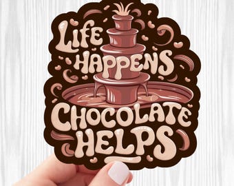 May include: A brown sticker with the text "Life Happens Chocolate Helps" in a whimsical font. The sticker features a chocolate fountain illustration. The background is a light wood grain pattern.
