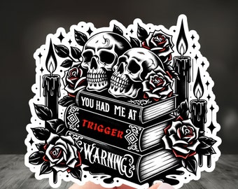 May include: Black and white sticker featuring two skulls with roses and candles on top of three books. The books have the text "You had me at", "Trigger", and "Warning" on their spines.