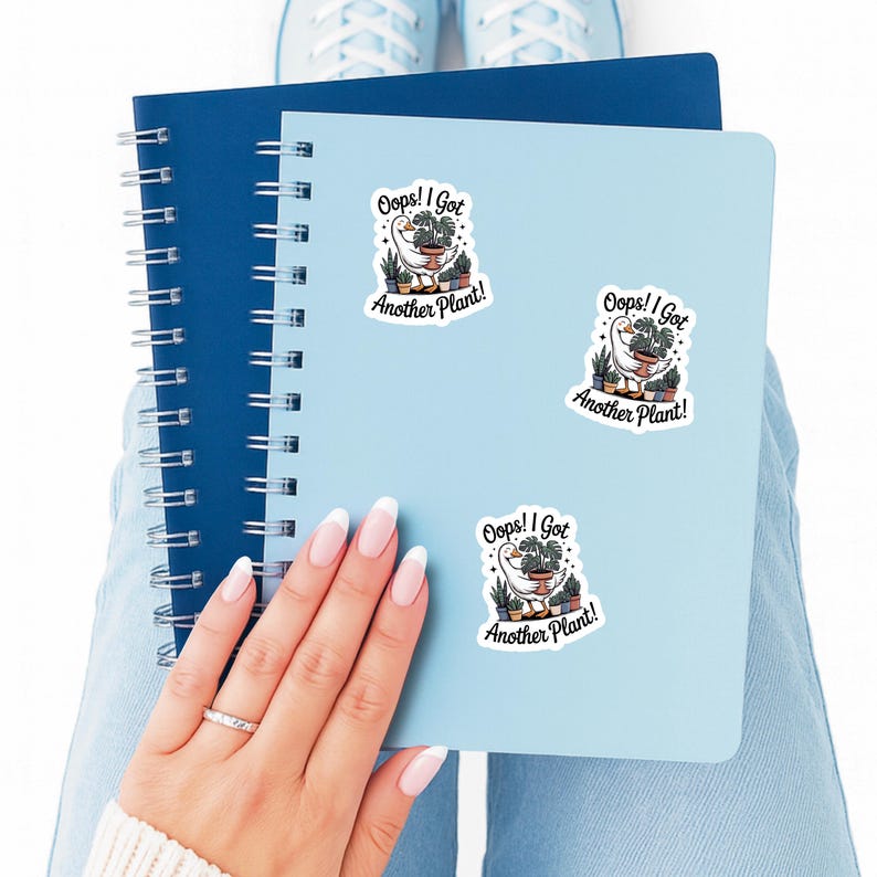 May include: A light blue notebook with spiral binding and a light blue notebook with three stickers that say "Oops! I Got Another Plant!" The stickers feature a goose with plants.