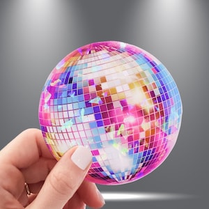 May include: A pink and purple disco ball with iridescent glitter. The disco ball is made of many small mirrored squares.
