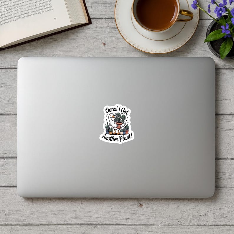 May include: A white sticker on a laptop featuring a cartoon goose holding a planter with various plants. The text reads "Oops! I Got Another Plant!" in a whimsical font, surrounded by a black border.