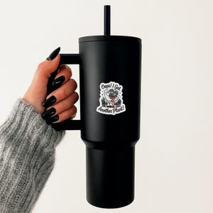 May include: Black insulated tumbler with a handle and a black straw. A white sticker on the tumbler reads "Oops! I Got Another Plant!" with a cartoon goose and potted plants. The tumbler is designed to keep beverages cold or hot.