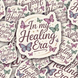 May include: A collection of stickers with a cream background, featuring the phrase "In my Healing Era" in a script font. The stickers are adorned with butterflies in shades of purple, blue, and green, creating a whimsical design.