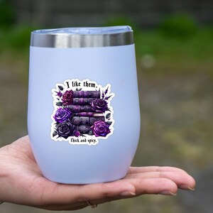 K&ouml;nnte beinhalten: Ein wei&szlig;er Edelstahlbecher mit einem Aufkleber, auf dem "I like them. Thick and spicy." steht. Der Aufkleber zeigt einen Stapel B&uuml;cher mit violetten und schwarzen Rosen.