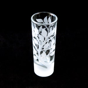 May include: A clear glass shot glass with a frosted bottom. The glass is etched with a white design of leaves and branches.