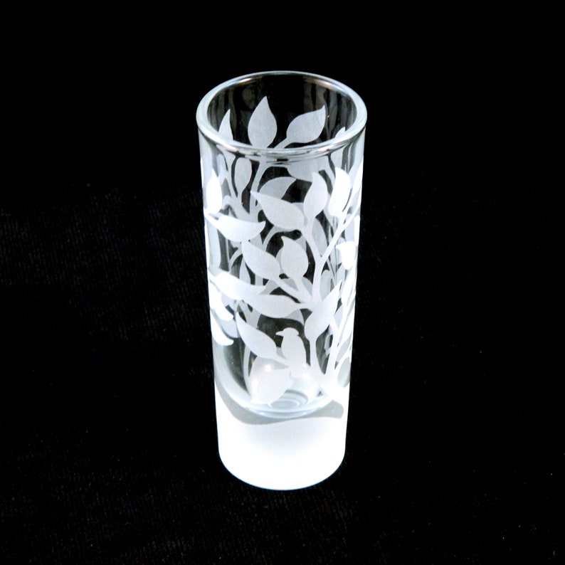 May include: A clear glass shot glass with a frosted bottom and a white etched design of leaves and branches.