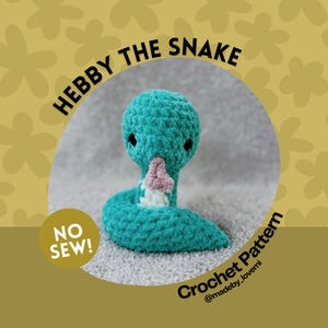 May include: A teal blue crocheted snake toy with a pink nose and black eyes. The toy is on a grey fuzzy surface. The text "Hebby the Snake" is in a circle above the toy. The text "No Sew!" is in a circle to the left of the toy. The text "Crochet Pattern @madeby_lovemi" is in a circle to the right of the toy.