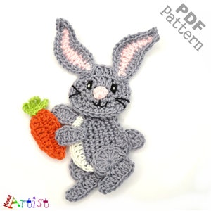 May include: A gray crocheted bunny holding a carrot. The bunny has pink ears and a white belly. The carrot is orange and green. The bunny is a crochet pattern.
