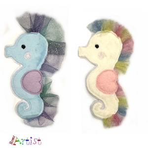 May include: Two felt seahorse ornaments with tulle skirts. One seahorse is light blue with a pink heart, the other is white with a pink heart. Both have rainbow tulle skirts.