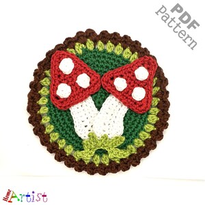 May include: Crochet pattern for two red and white mushrooms with white stems, surrounded by green and brown crocheted leaves. The pattern is available as a PDF download.