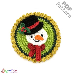 May include: Crocheted snowman ornament with a black hat, red scarf, and green holly. The snowman is surrounded by a green and gold crocheted circle.