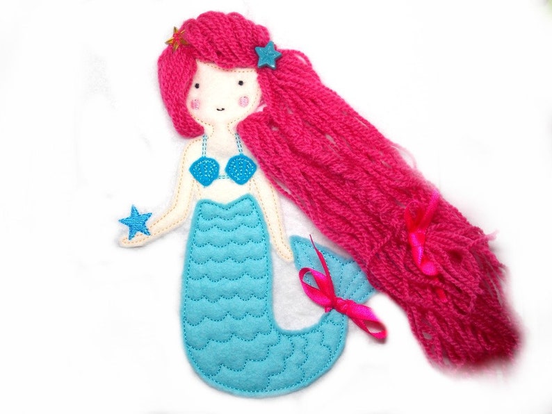 May include: A felt mermaid doll with pink yarn hair, a blue top, and a turquoise tail. The doll is holding a blue star.