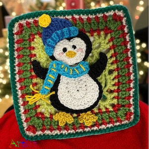 May include: A crocheted square with a penguin motif. The penguin has a white belly, black wings, and wears a blue hat and scarf. The square has a green and red border, with yellow accents. The design has a festive theme.