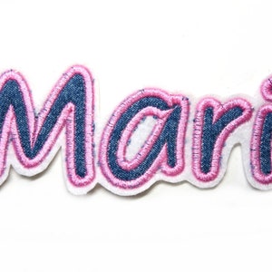 Könnte beinhalten: Ein gestickter Bügelaufkleber in Pink und Blau mit dem Namen "Mari" in einer kursivschrift.