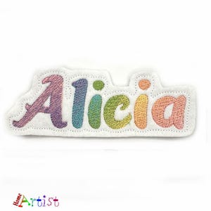 May include: A white felt patch with the name "Alicia" embroidered in rainbow colors.