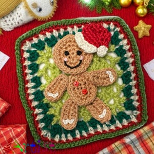 May include: A crocheted gingerbread man wearing a Santa hat, placed on a square coaster with green, red, and white crochet detailing. The gingerbread man has a smiling face and red button details. The coaster is on a red surface.