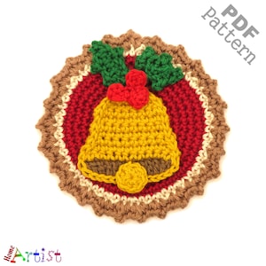 Puede incluir: Adorno navideño de crochet con un círculo rojo y blanco con una campana amarilla y hojas de acebo verdes. El adorno está rodeado por un borde de crochet marrón.