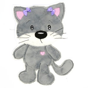 May include: A gray plush cat with pink ears and purple bows. The cat has a white face with black eyes and a black nose. It has a pink heart on its chest.