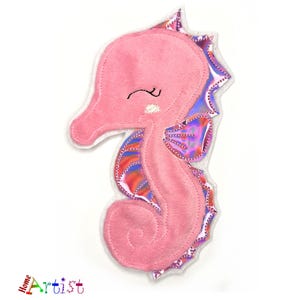 May include: Pink felt seahorse applique with iridescent purple and orange details. The seahorse has a smiling face with closed eyes.