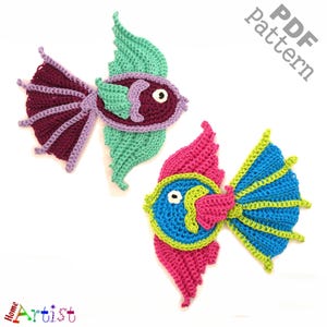 May include: Two crocheted fish appliques featuring intricate yarn work. One fish is dark purple with mint green fins and tail, while the other is blue with bright pink and lime green accents. Both have white eyes. Text reads PDF Pattern.