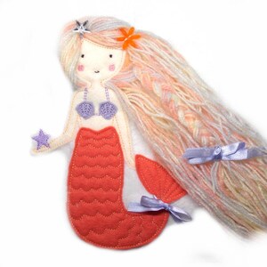 May include: A felt mermaid doll with long pink and white yarn hair, a purple seashell bra, and a red tail with a star in her hand.