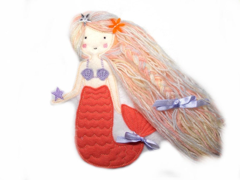 May include: A felt mermaid doll with long pink and white yarn hair, a purple seashell bra, and a red tail with a star in her hand.