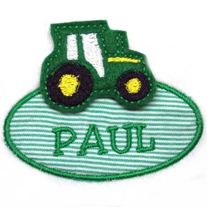 Puede incluir: Aplique de tractor verde y amarillo en un parche de tela ovalado a rayas verdes y blancas con el nombre "PAUL" bordado en blanco.