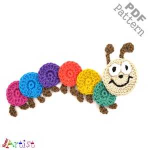 May include: A colourful crocheted caterpillar with a smiling face. The caterpillar is made of six circles in different colours: pink, blue, purple, red, yellow, and green. The head is beige with black eyes and a black smile.
