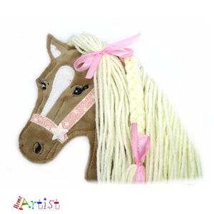 Könnte beinhalten: Ein brauner Pferdekopf mit einem weißen Stern auf der Stirn, einem rosafarbenen Zaumzeug und einer langen, blonden Mähne mit einem rosafarbenen Band, das zu einer Schleife gebunden ist. Die Mähne ist auf einer Seite geflochten.