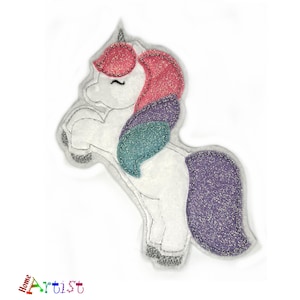 Peut inclure: Une applique de licorne blanche avec des accents rose, violet et turquoise. La licorne a une queue violette scintillante et une crinière rose.