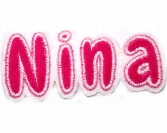 May include: Pink felt name patch with the name "Nina" in white outline.