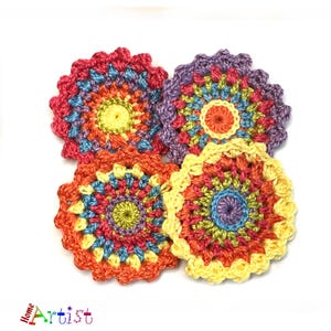 May include: Four crocheted colorful flower-shaped coasters with a multi-colored center. The coasters are made with a variety of shades of orange, yellow, red, blue, green, and purple yarn.