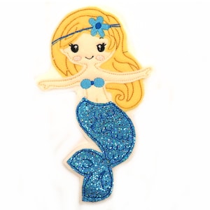 Puede incluir: Una aplicación de fieltro de una sirena con cabello rubio, una cola azul con brillo y un sujetador de concha azul.