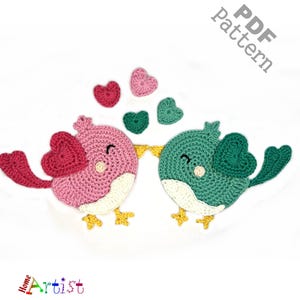 May include: Crochet pattern for two lovebirds holding hearts. The pattern is available as a PDF download. The birds are pink and green with yellow feet.
