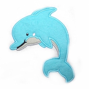 May include: A light blue felt dolphin applique with a white and gray accent. The dolphin has a smiling face and a curved tail. This applique is suitable for various craft projects.
