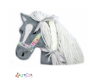 May include: Gray horse head plush toy with a rainbow heart patterned bridle and a white yarn mane and tail. The mane is braided and tied with a silver ribbon.
