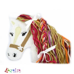 May include: A white felt horse head with a brown bridle and a star accent. The horse has a colorful yarn mane in shades of red, orange, and gold, accented with white bows. The logo "Home Artist" is visible.