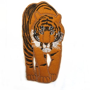May include: An embroidered tiger patch in brown and black with white accents. The tiger is facing forward with its mouth closed.