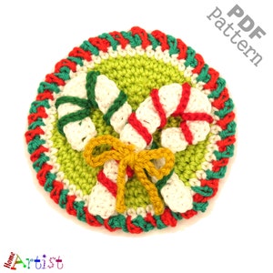 May include: A crocheted Christmas coaster featuring a green center with white, red, and green candy canes and a yellow bow. The coaster has a red, white, and green border. The words "PDF Pattern" are in the upper right corner.