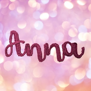 May include: A dark magenta crochet word art piece spelling the name Anna in a cursive, connected script font. The letters are formed from a single continuous strand of yarn with a visible, textured, looped stitch pattern throughout the entire design.