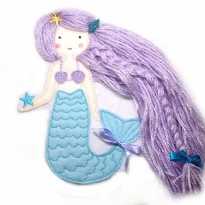 May include: A felt mermaid doll with a purple yarn wig, a blue and white seashell bra, a blue tail with a blue and white seashell pattern, and a blue star in her hand.