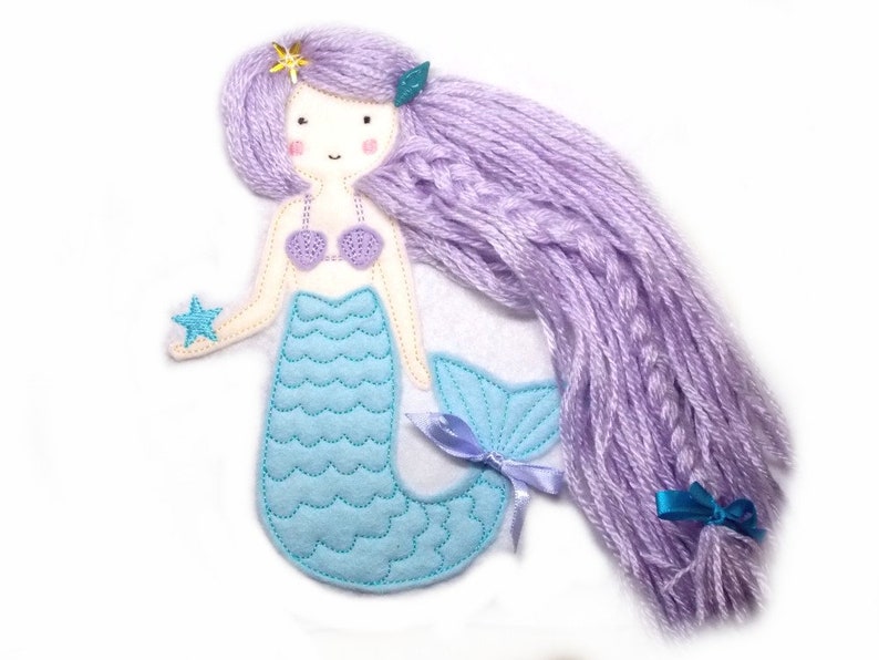 May include: A felt mermaid doll with a purple yarn wig, a blue and white seashell bra, a blue tail with a blue and white seashell pattern, and a blue star in her hand.