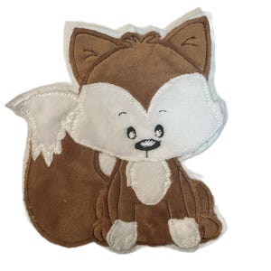 Könnte beinhalten: Eine Stoffapplikation in Form eines Fuchses mit braunen und weißen Plüschabschnitten. Der Fuchs hat gestickte schwarze Augen, eine kleine schwarze Nase und einen weißen Brustfleck. Die Ränder sind mit weißen Nähten versehen.