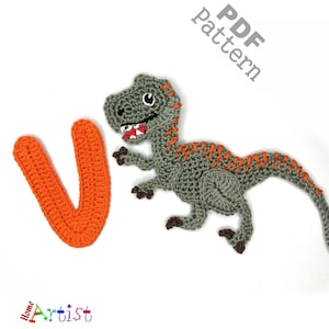 May include: A crocheted dinosaur and the letter "V" in orange. The dinosaur is grey with orange stripes and a red mouth. The image has the text "PDF pattern" and "Home Artist".