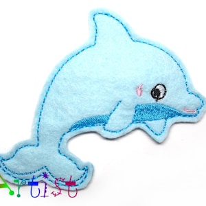 May include: A light blue felt dolphin applique with embroidered details. The dolphin has a smiling pink mouth, a blue embroidered belly, and a black and white eye. Suitable for crafts or sewing projects.