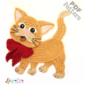Puede incluir: Aplique de gato de ganchillo con un lazo rojo. El gato es de color canela con la nariz rosa y bigotes negros. El patrón está disponible para descargar en PDF.