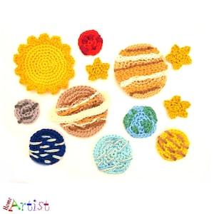 Puede incluir: Un conjunto de sistema solar tejido a crochet con un sol amarillo, planetas rayados de color marrón y blanco, planetas azules y blancos y un planeta rojo. También hay estrellas amarillas y naranjas.