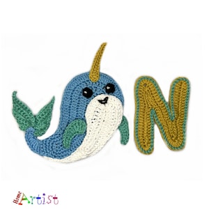 May include: Crocheted narwhal with a gold horn and green fins, next to a crocheted letter N in yellow and green.