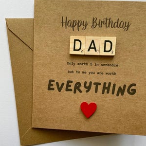 May include: A square brown kraft paper birthday card featuring the text Happy Birthday and DAD spelled out with wooden letter tiles. Below the tiles, the text reads Only worth 5 in scrabble but to me you are worth EVERYTHING, with a small red heart.